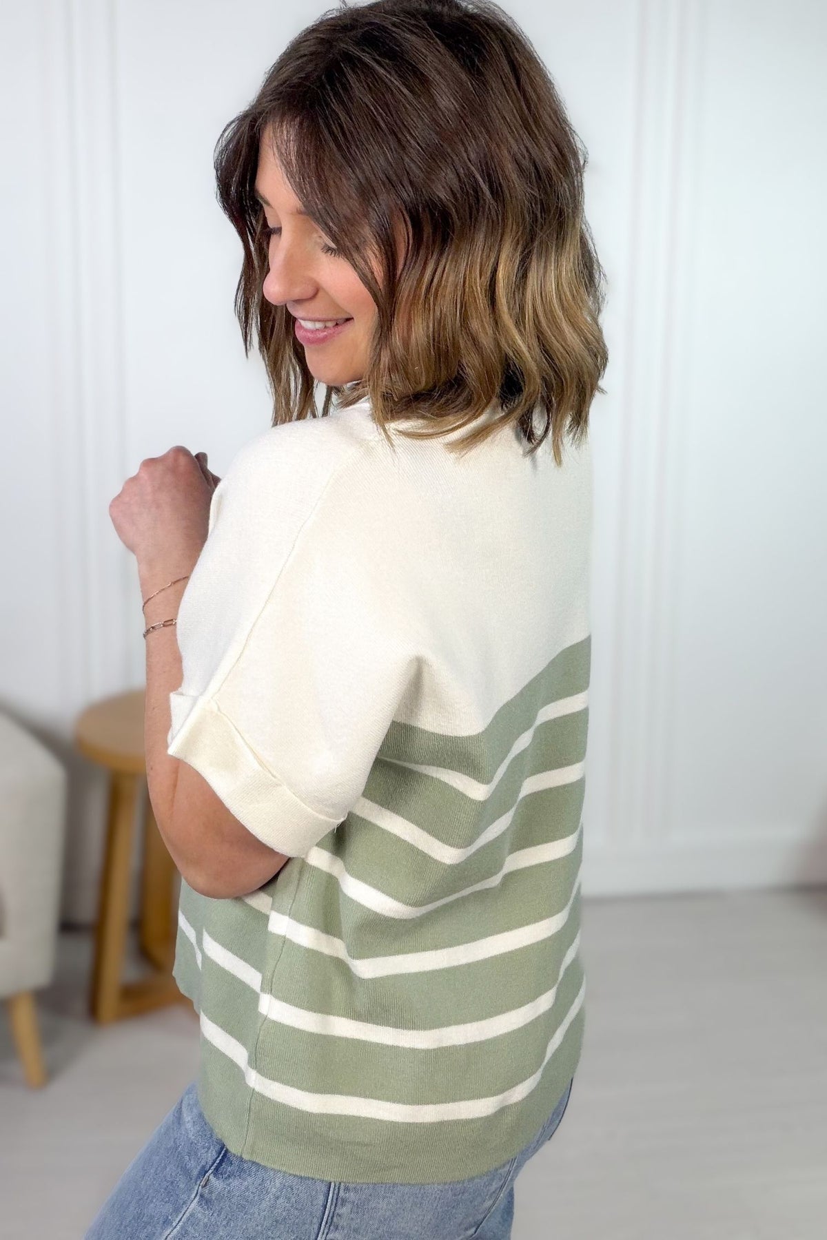 Woman wearing a green and white striped shirt in a room with a white wall and wooden floor showing back and side details.