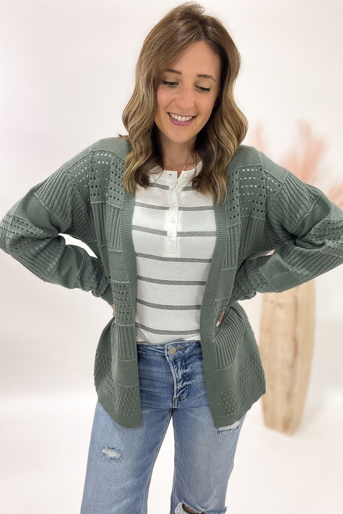 Woman wearing a green cardigan over a striped shirt with a white background