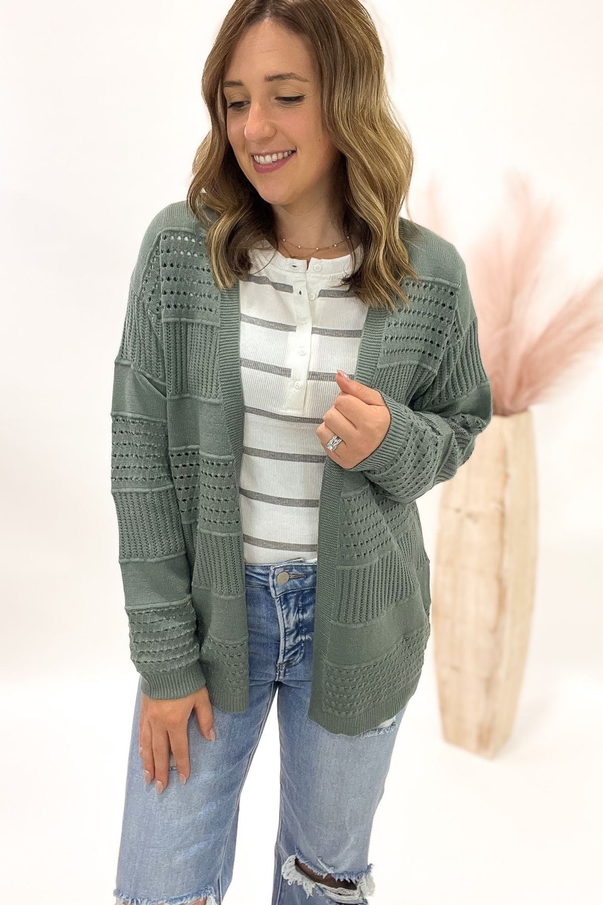 Woman wearing a green cardigan over a striped shirt with a white background