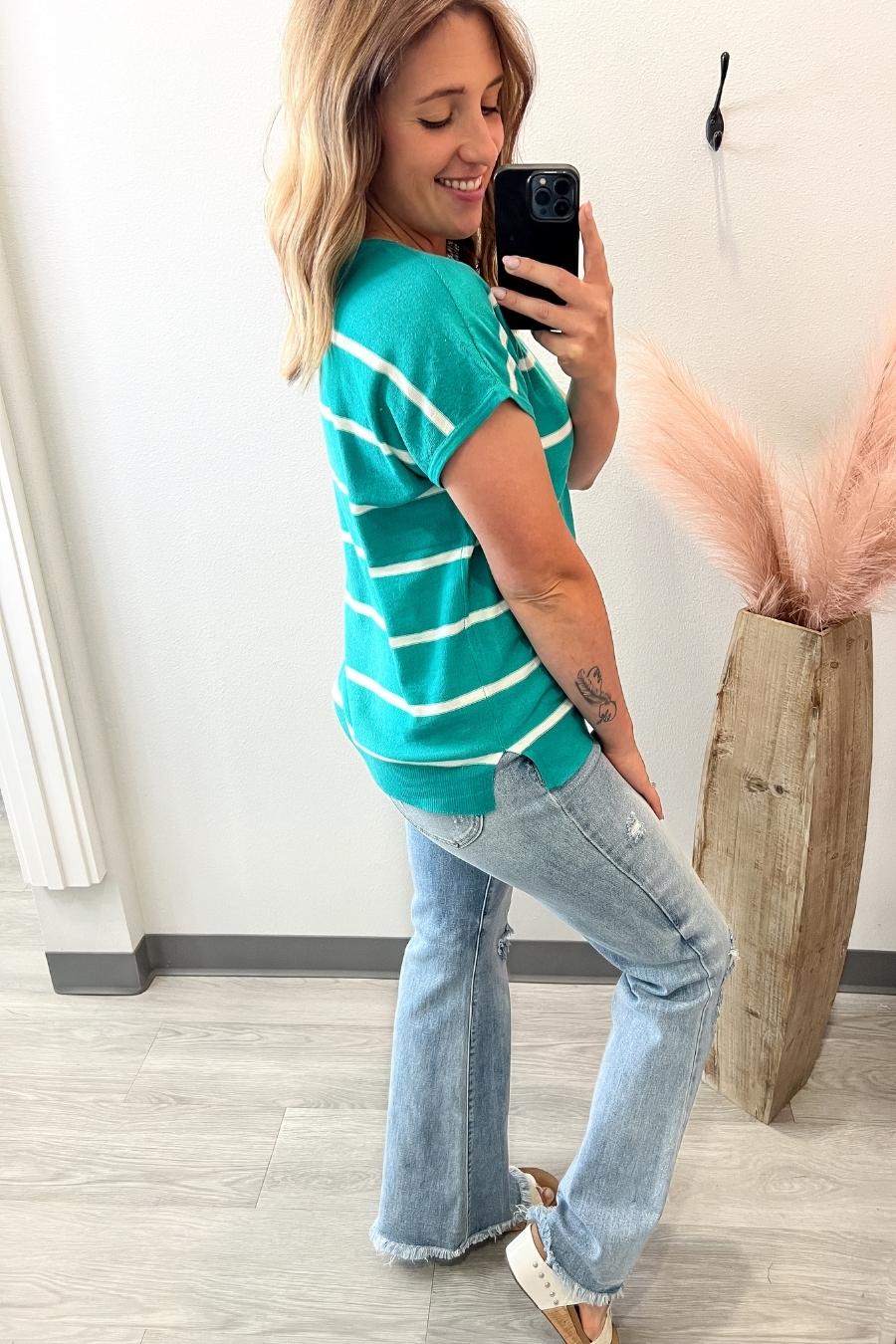 Woman taking a selfie in a green striped shirt and jeans indoors.