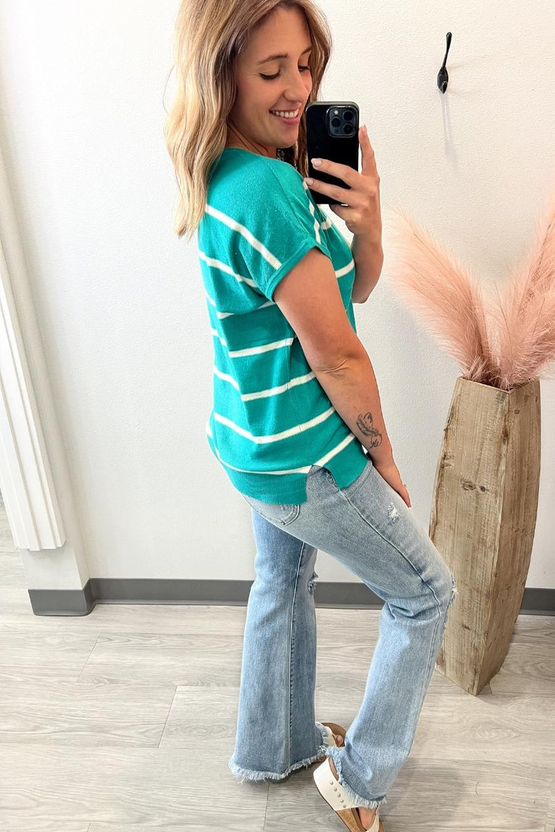Woman taking a selfie in a green striped shirt and jeans indoors.