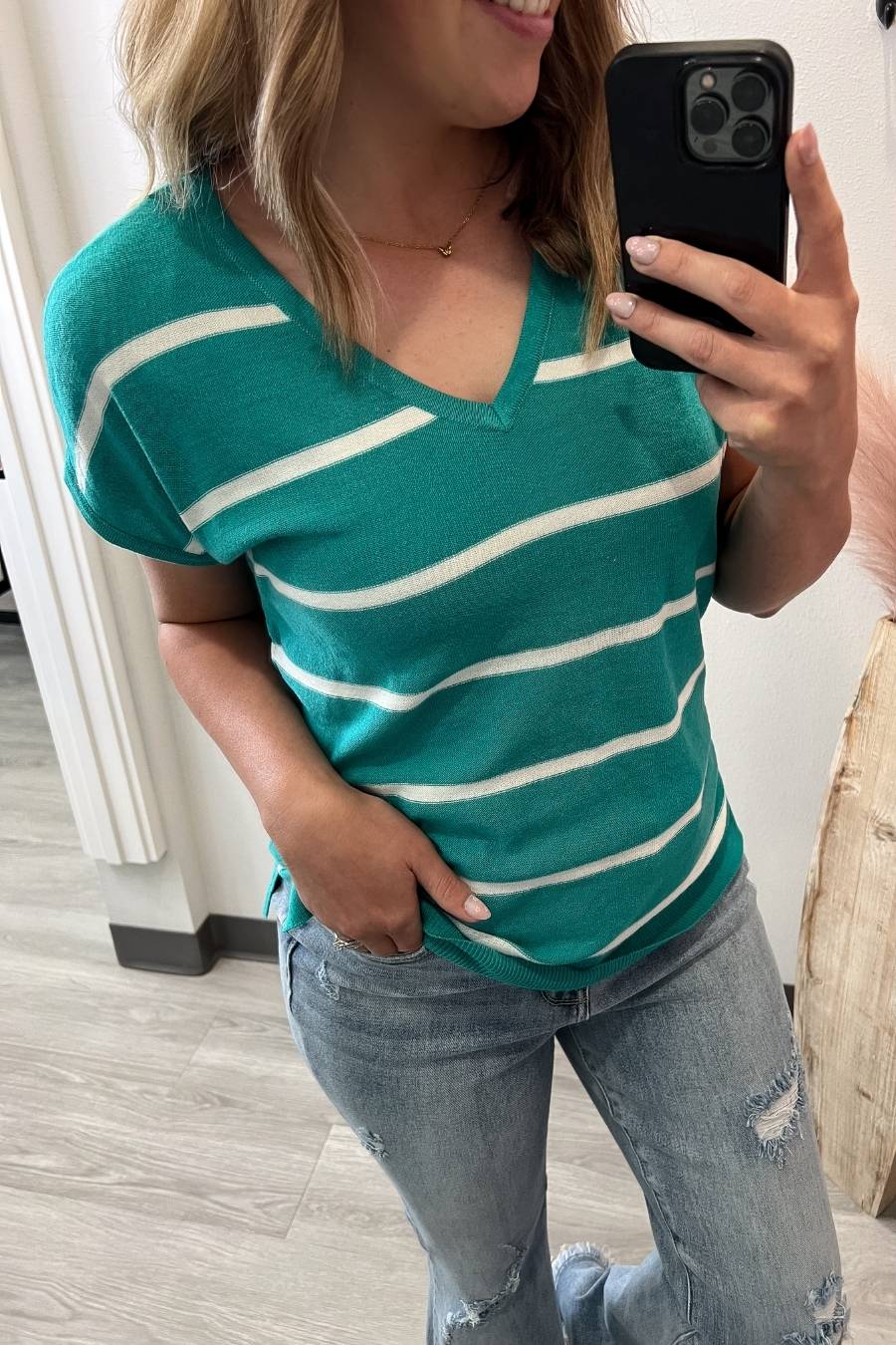 Person wearing a green and white striped shirt and blue jeans, taking a mirror selfie.