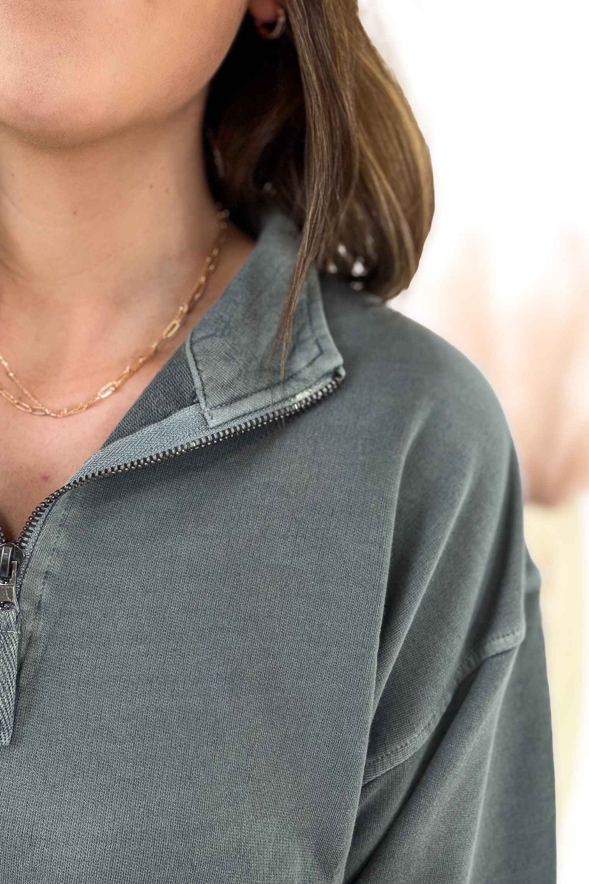 Close-up of a person wearing a jade half zip pullover with a blurred background