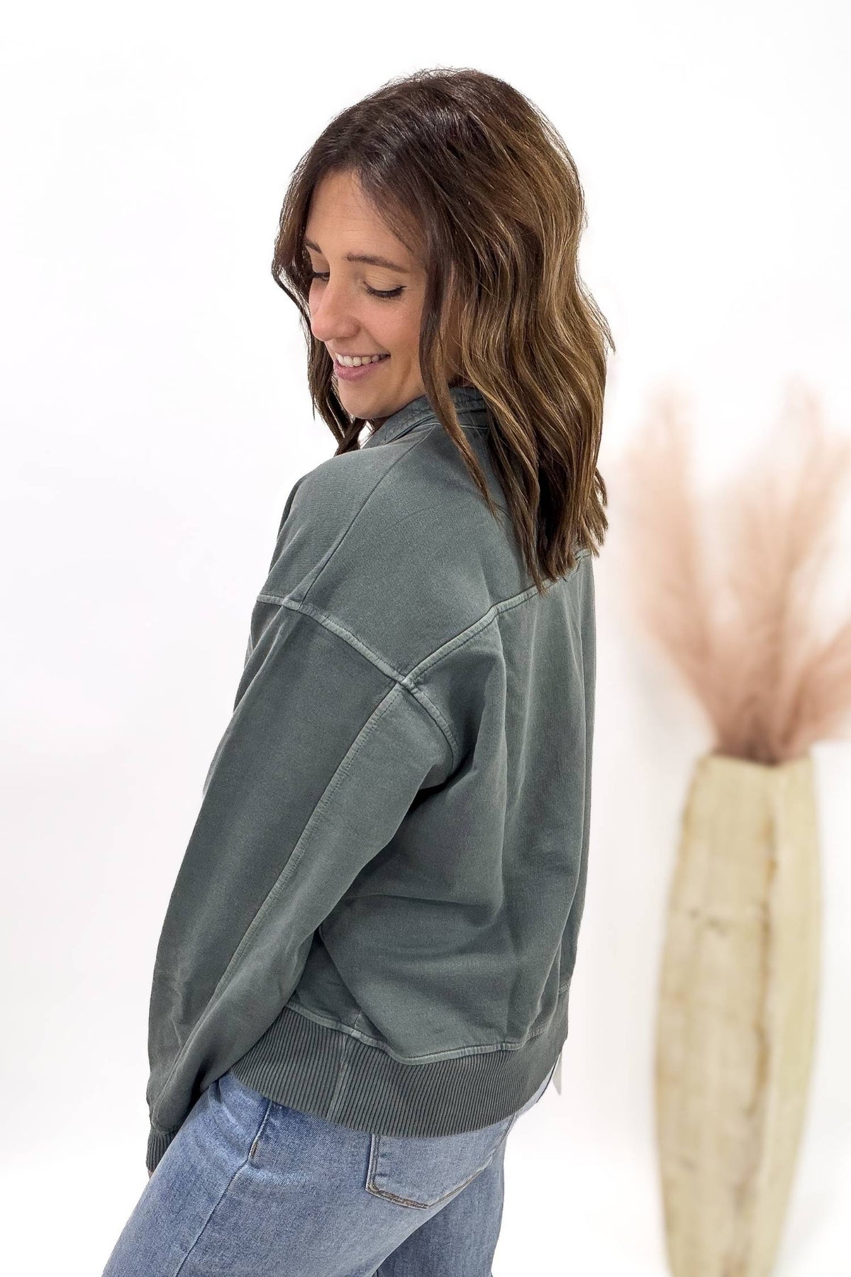 Woman wearing a jade pullover and blue jeans on a white background