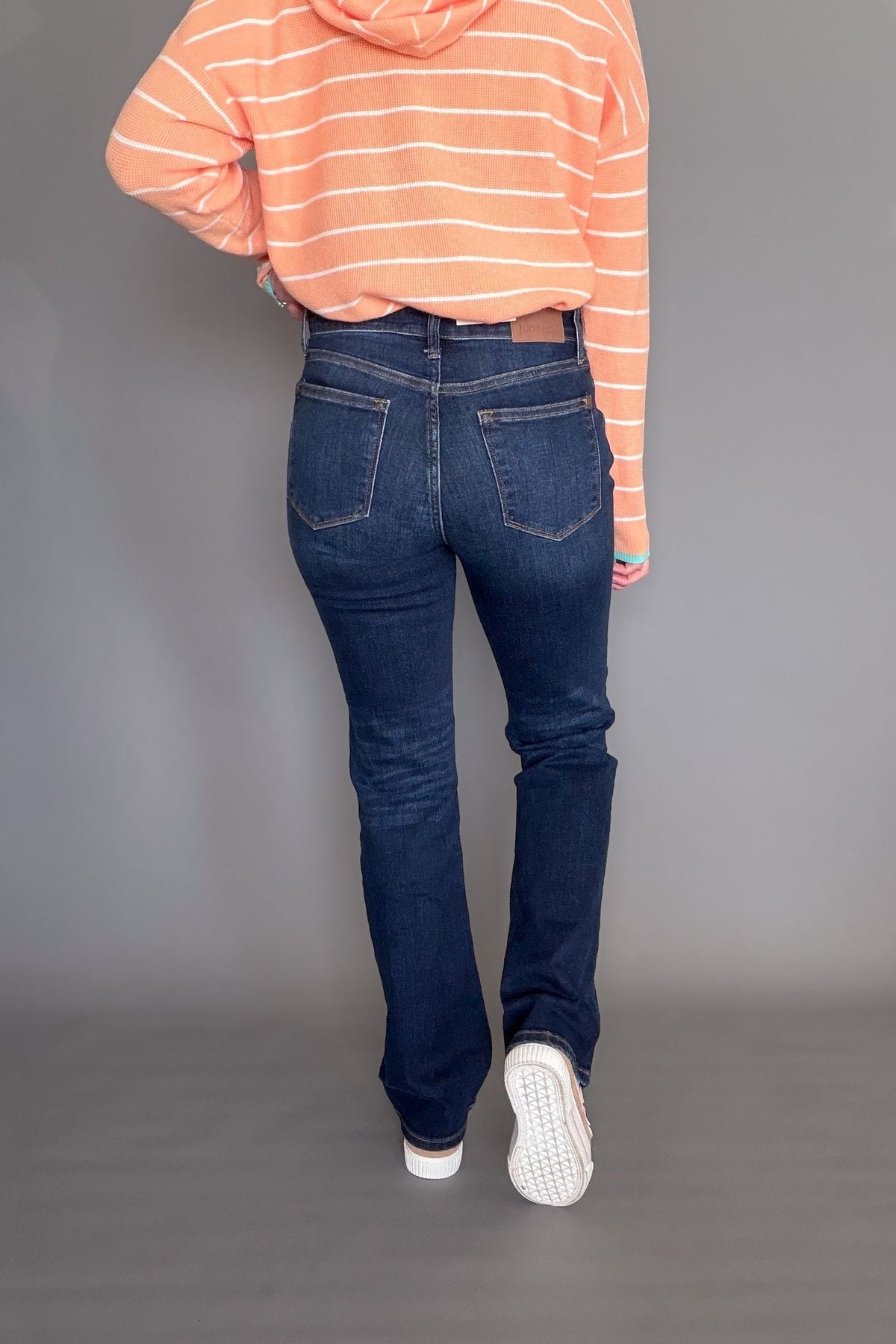 Person wearing blue jeans and an orange striped hoodie on a gray background