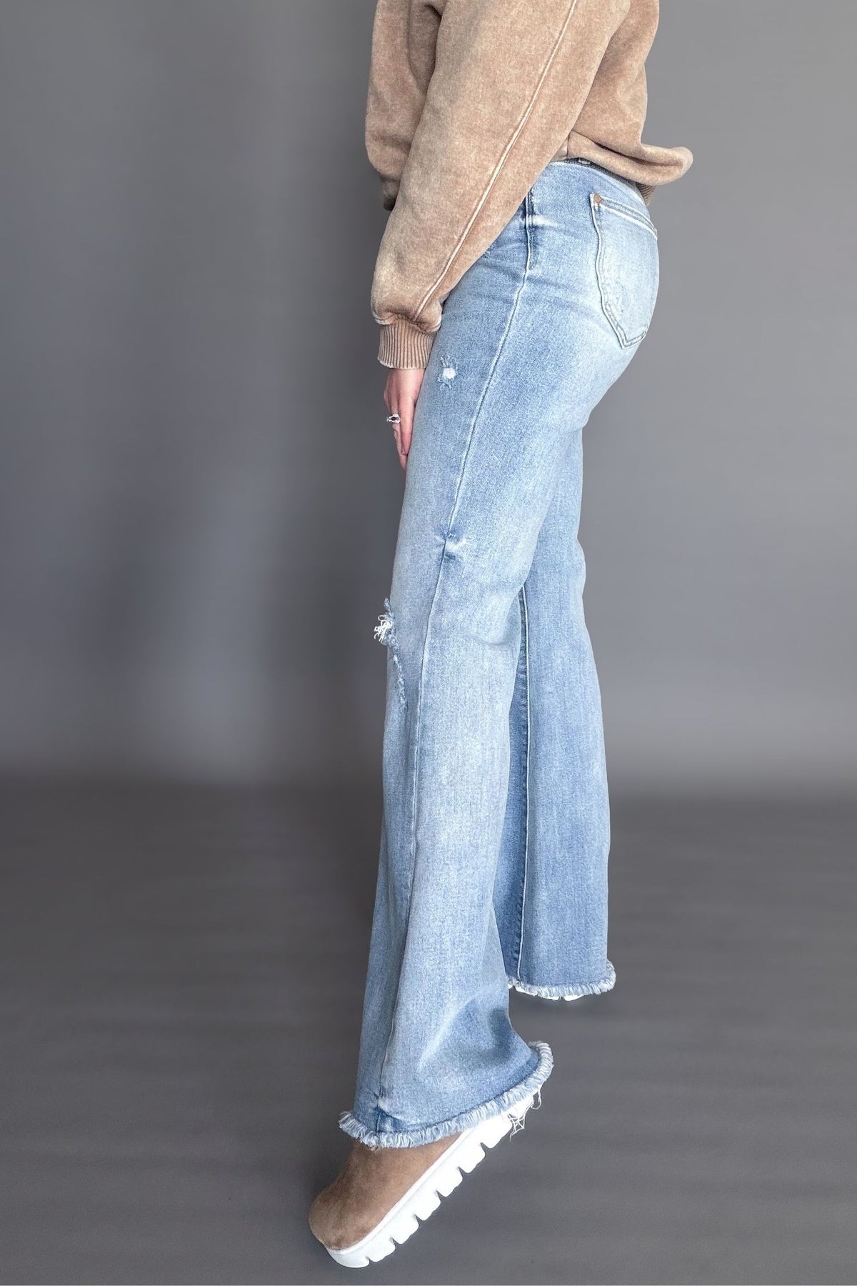 Person wearing light blue jeans and brown shoes on a gray background