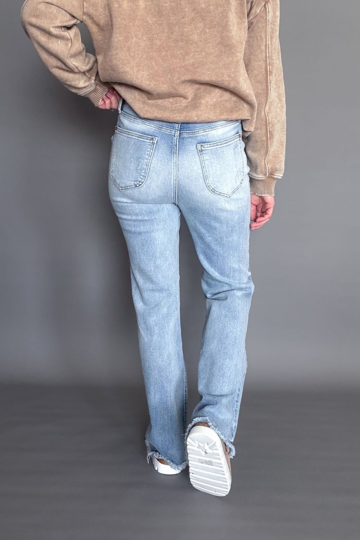 Person wearing a brown sweatshirt and light blue jeans on a gray background