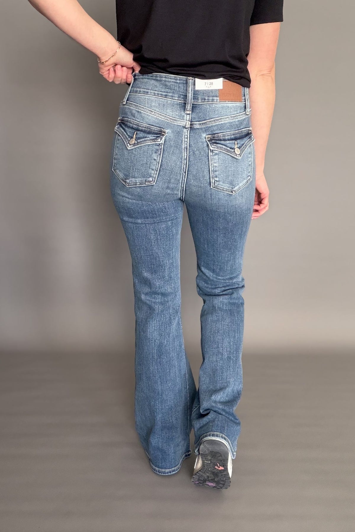 Person wearing blue jeans and a black shirt on a plain background showing the back of the denim. (pocket flap details)