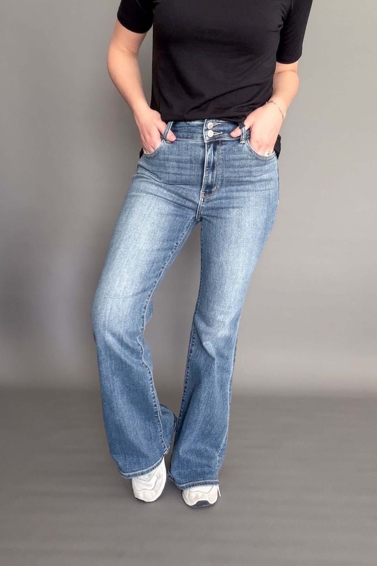 Person wearing blue flared jeans and a black top on a gray background