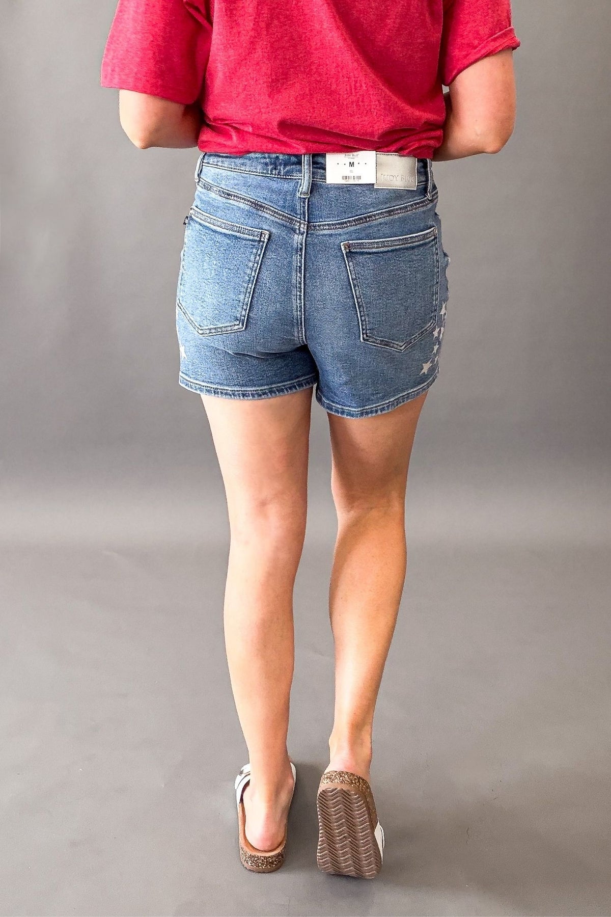 Woman wearing Judy Blue high waist slim denim shorts with white star spatter detail showing the back details