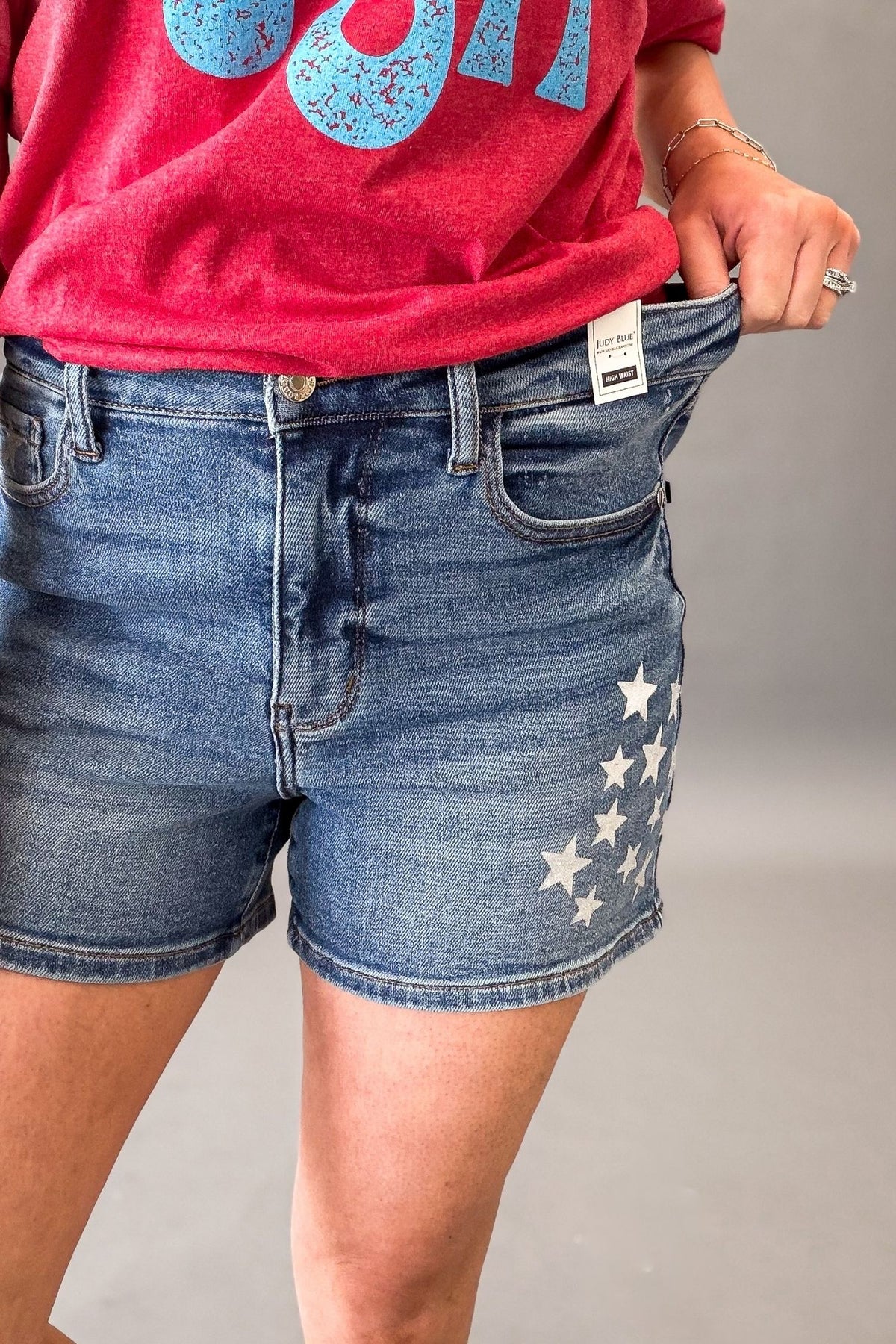 Woman wearing Judy Blue high waist slim denim shorts with white star spatter detail showing stretch in the waistband