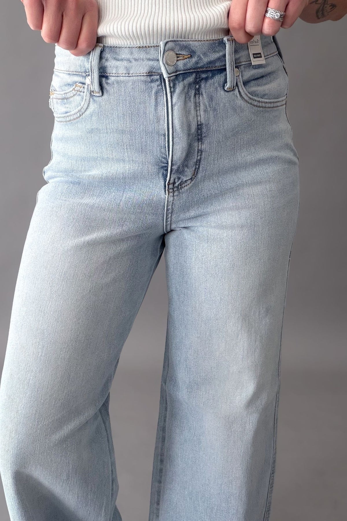 Judy Blue light wash vintage wide jean with high waist and tummy control worn with white wedges and a white tank on a grey background
