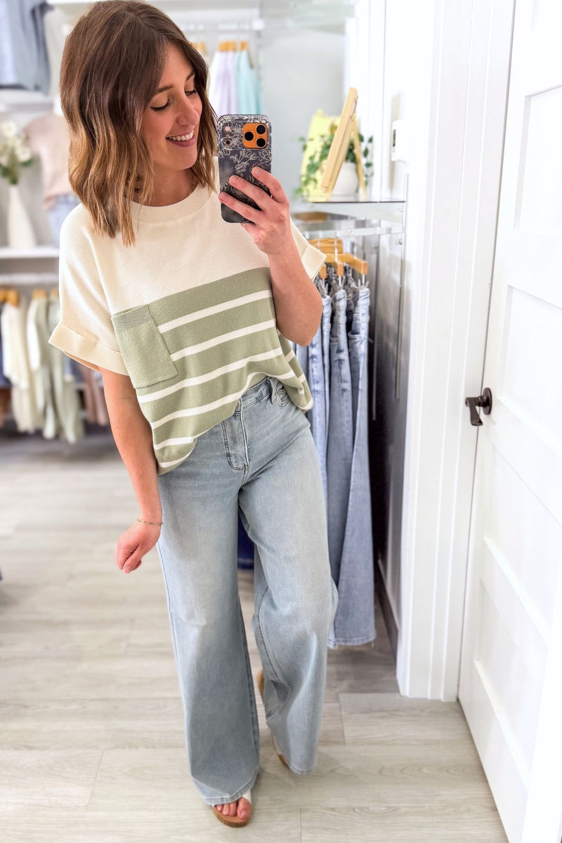 Woman taking a mirror selfie wearing a striped shirt and judy blue wide leg jeans in the boutique.