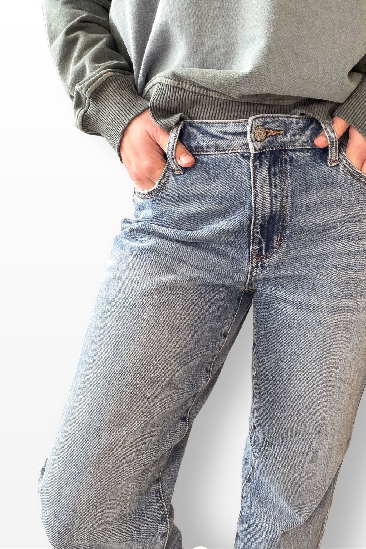 Person wearing light blue jeans and a green sweatshirt on a white background