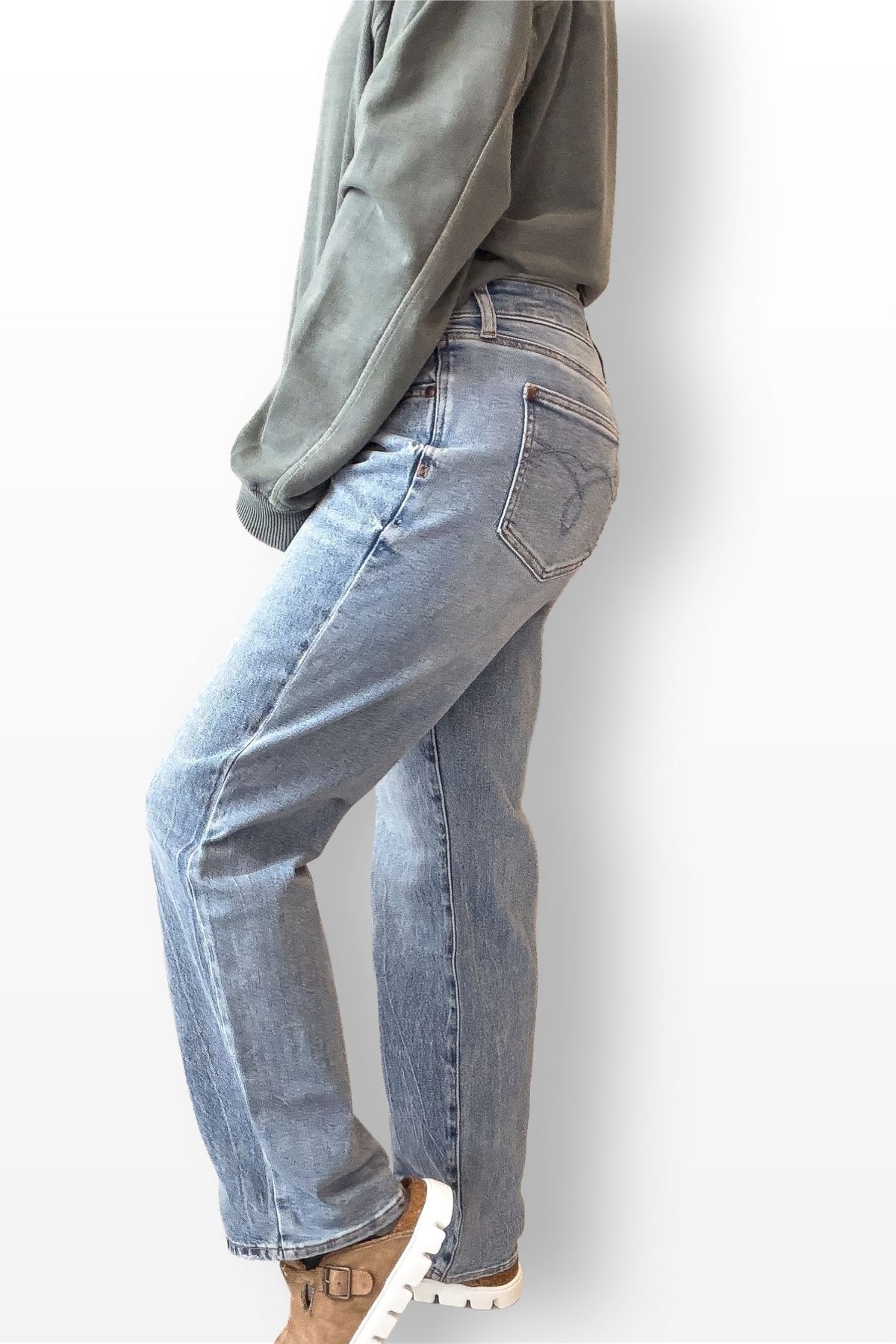 Person wearing light blue jeans and a green sweatshirt on a white background
