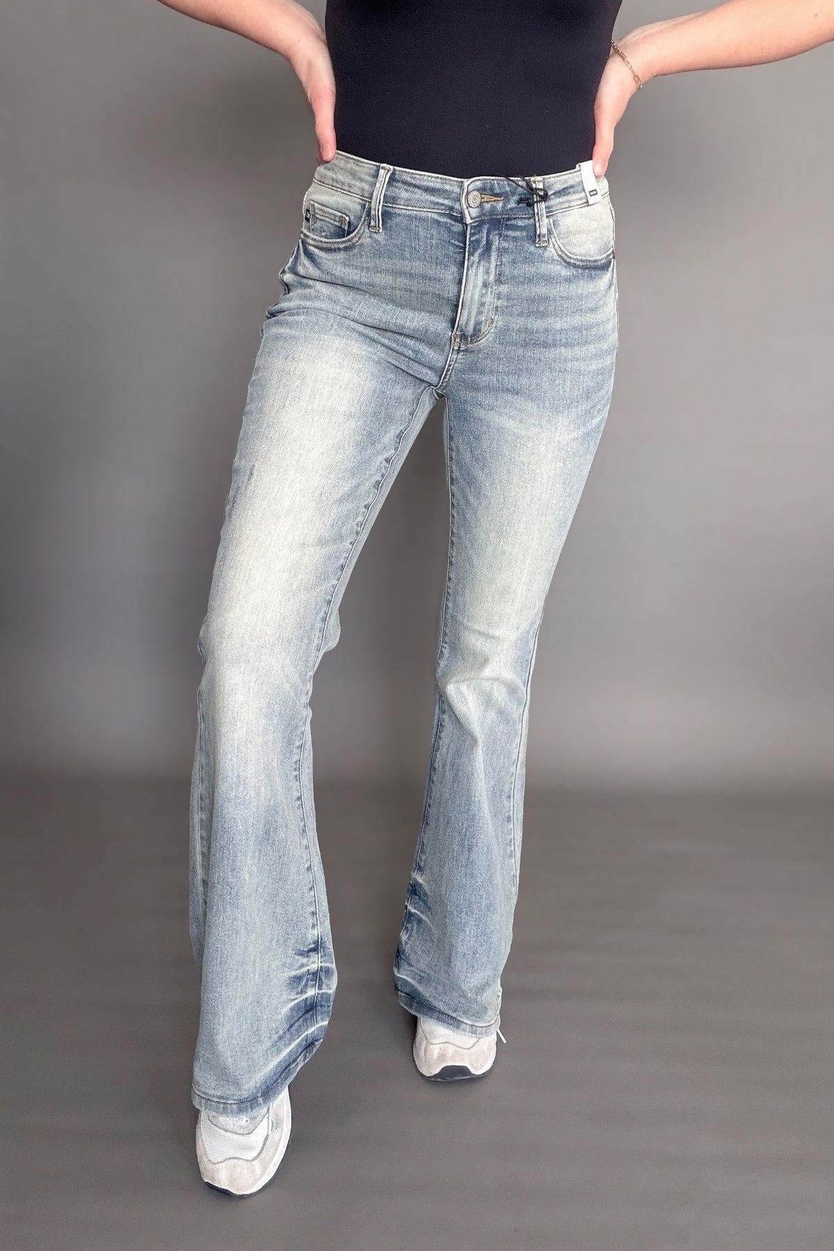 Person wearing light blue flared jeans on a gray background