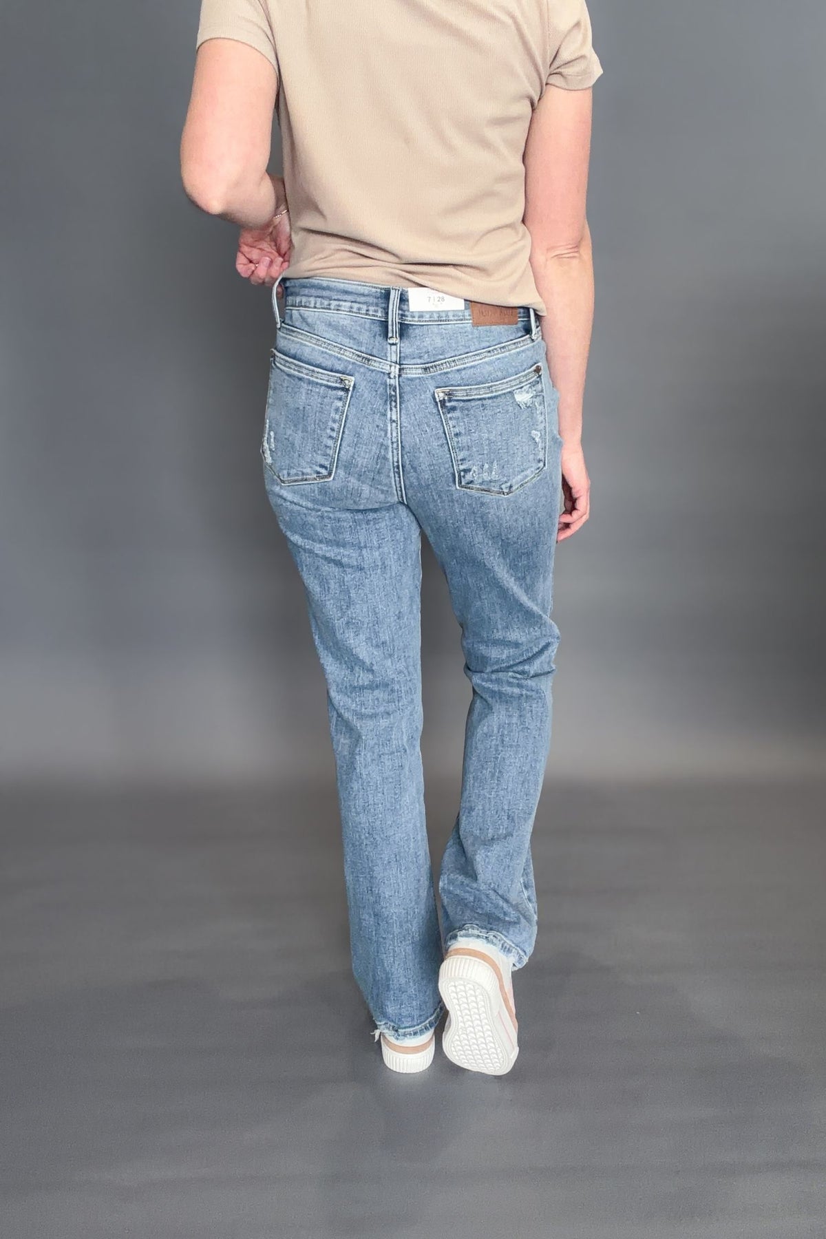 Person wearing a pair of Judy Blue Sabrina Mid Rise Vintage Wash Boot Cut Jeans with a beige short sleeve on a grey background (showing the back of the jeans)