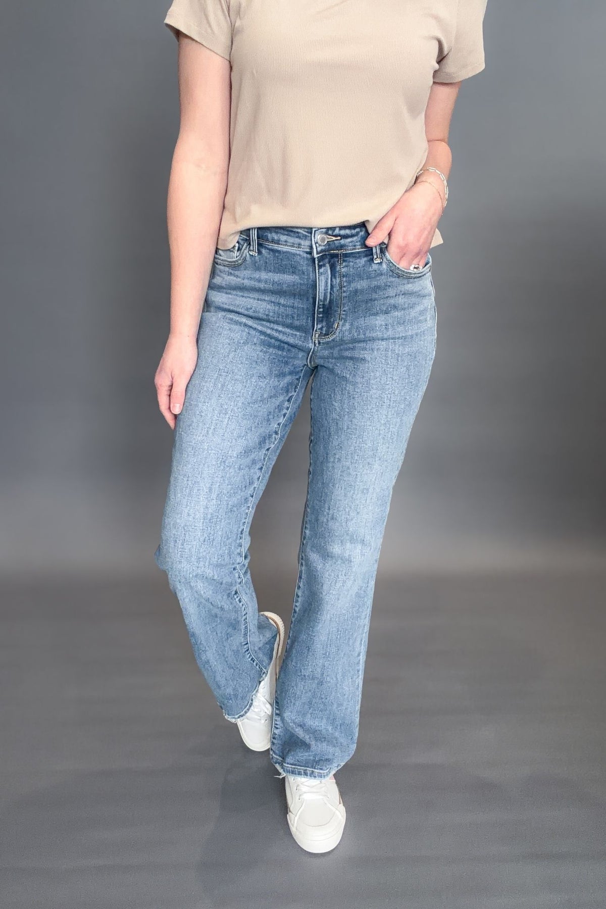 Person wearing a pair of Judy Blue Sabrina Mid Rise Vintage Wash Boot Cut Jeans with a beige short sleeve on a grey background