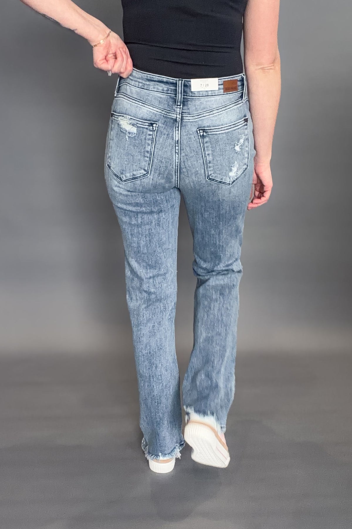 Woman wearing Judy Blue Sandra Destroyed Mid Rise Straight with a black tank and white sneakers on a grey background showing back of denim jeans