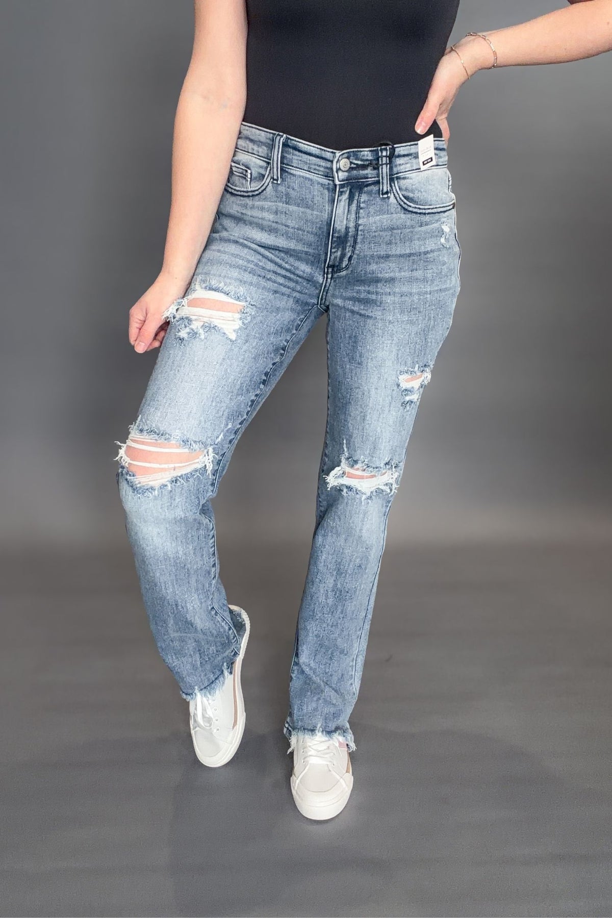 Woman wearing Judy Blue Sandra Destroyed Mid Rise Straight with a black tank and white sneakers on a grey background showing front view of denim jeans