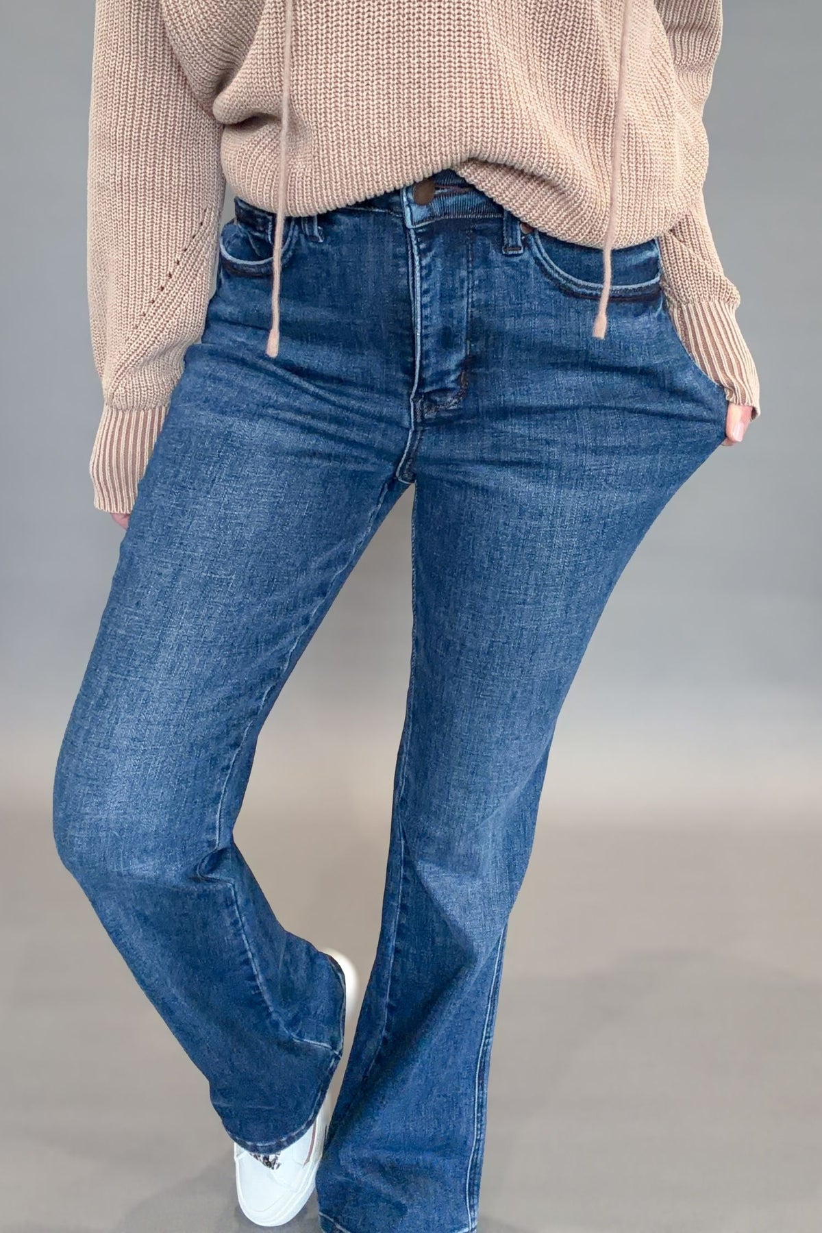 Person wearing judy blue jeans and a beige sweater on a gray background