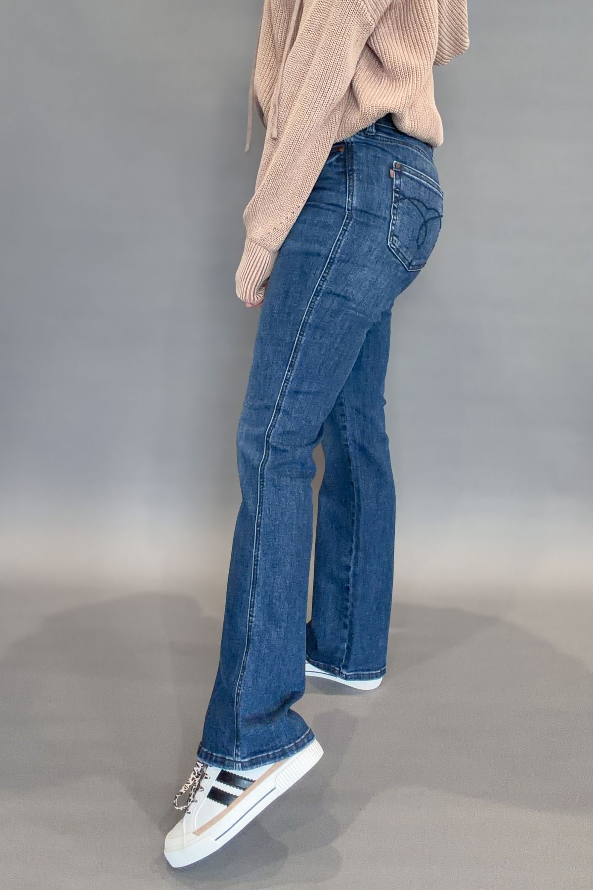 Person wearing judy blue jeans and a beige sweater on a gray background