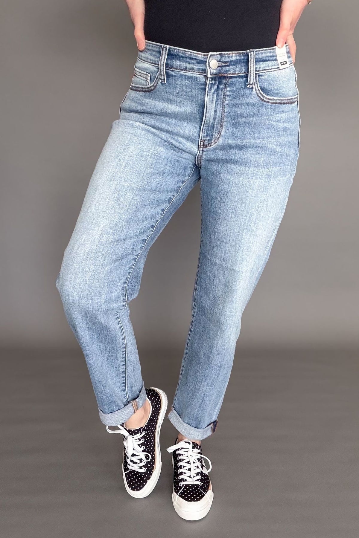 Woman wearing Judy Blue mid rise boyfriend jeans in light wash denim styled cuffed with black sneakers.