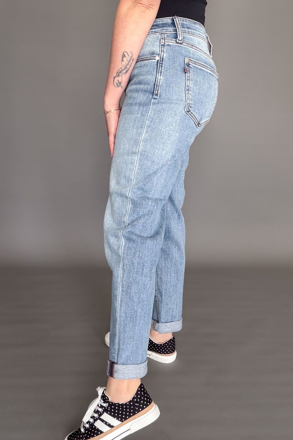 Woman wearing Judy Blue mid rise boyfriend jeans in light wash denim styled cuffed with black sneakers showing the side view