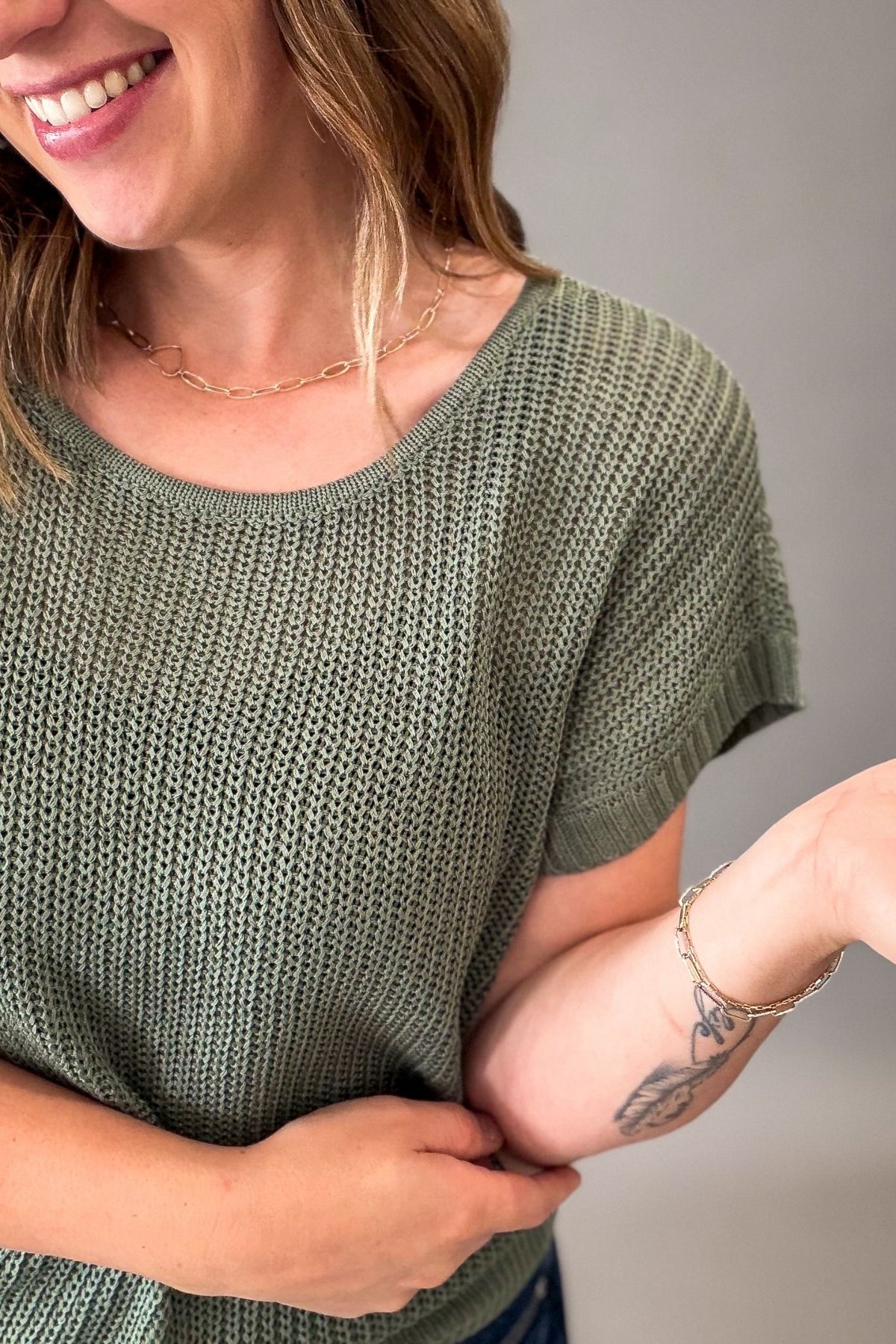 A close-up of a woman wearing a textured emerald green short-sleeve knit top, showing the ribbed fabric and scoop neckline.