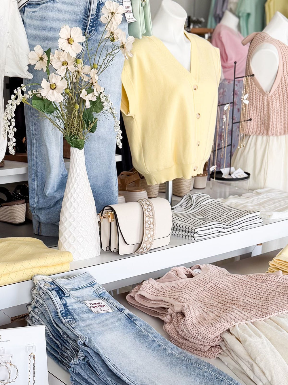 Display of clothing and accessories in a store with jeans, handbags, and dresses.