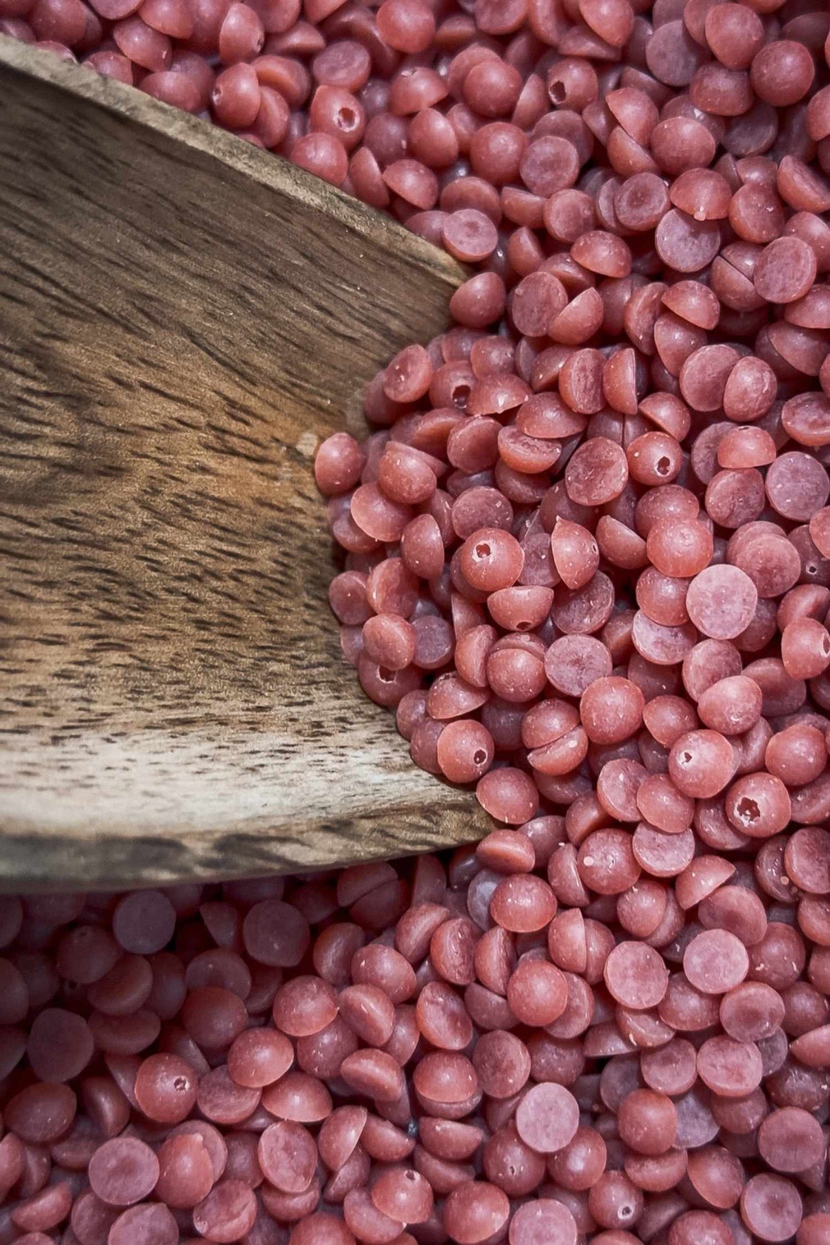 Close-up of pink wax beads with a wooden spoon