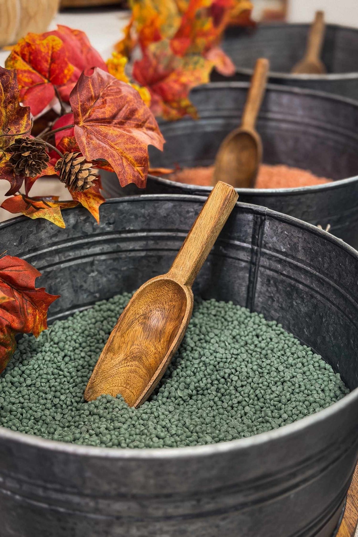 Decorative setup with wooden scoop, green beads, and autumn leaves in a black container.