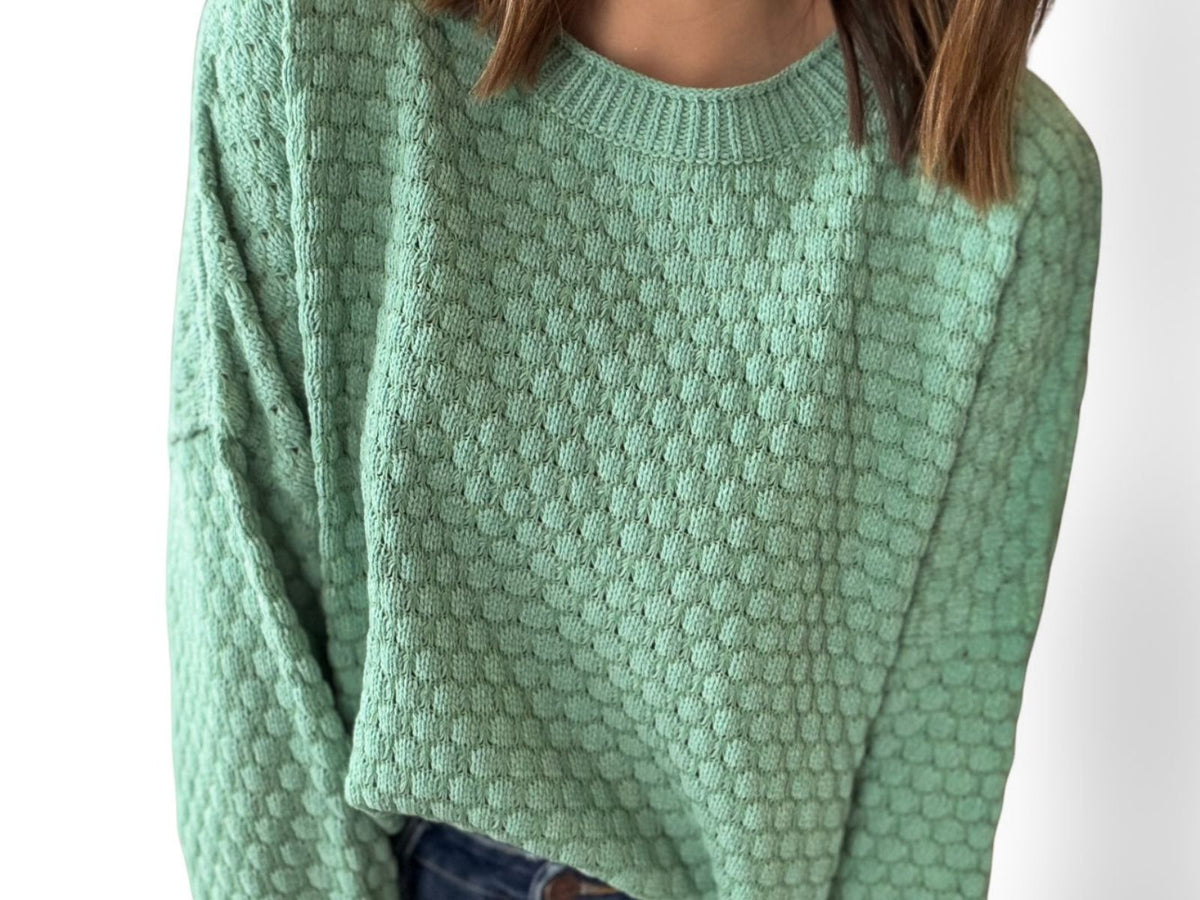 Green knitted sweater worn by a person on a white background