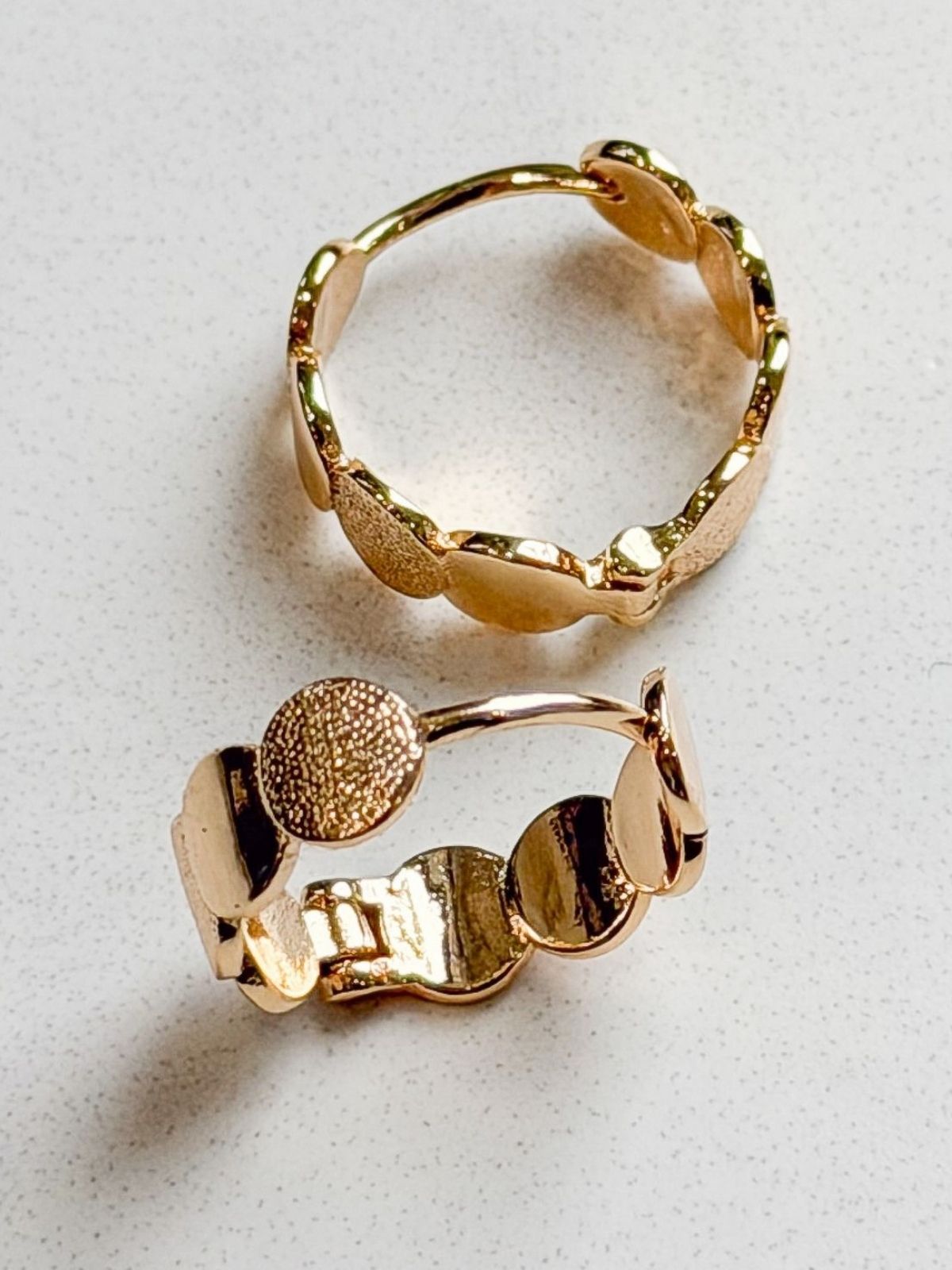 Two gold earrings on a light gray surface