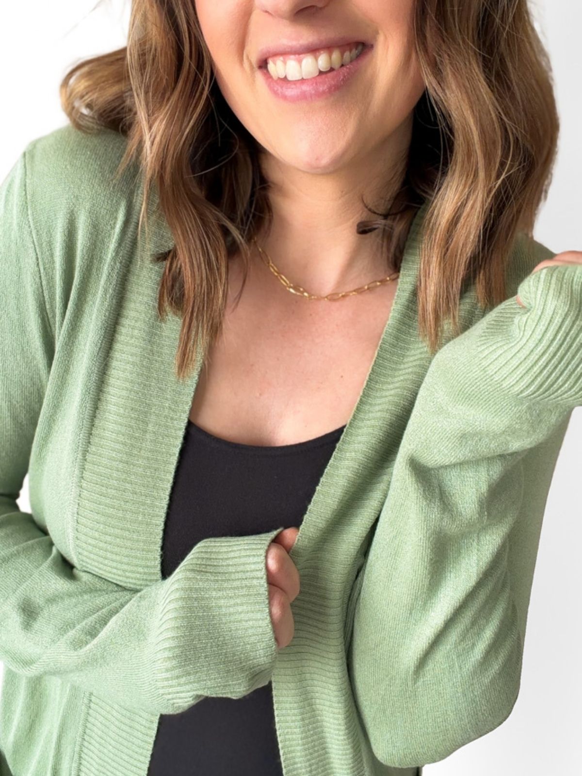Woman wearing a green cardigan over a black top on a white background