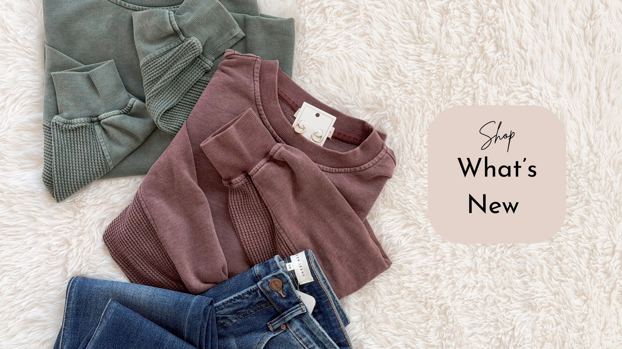 Two sweaters and a pair of jeans on a textured surface with 'Shop What's New' text.