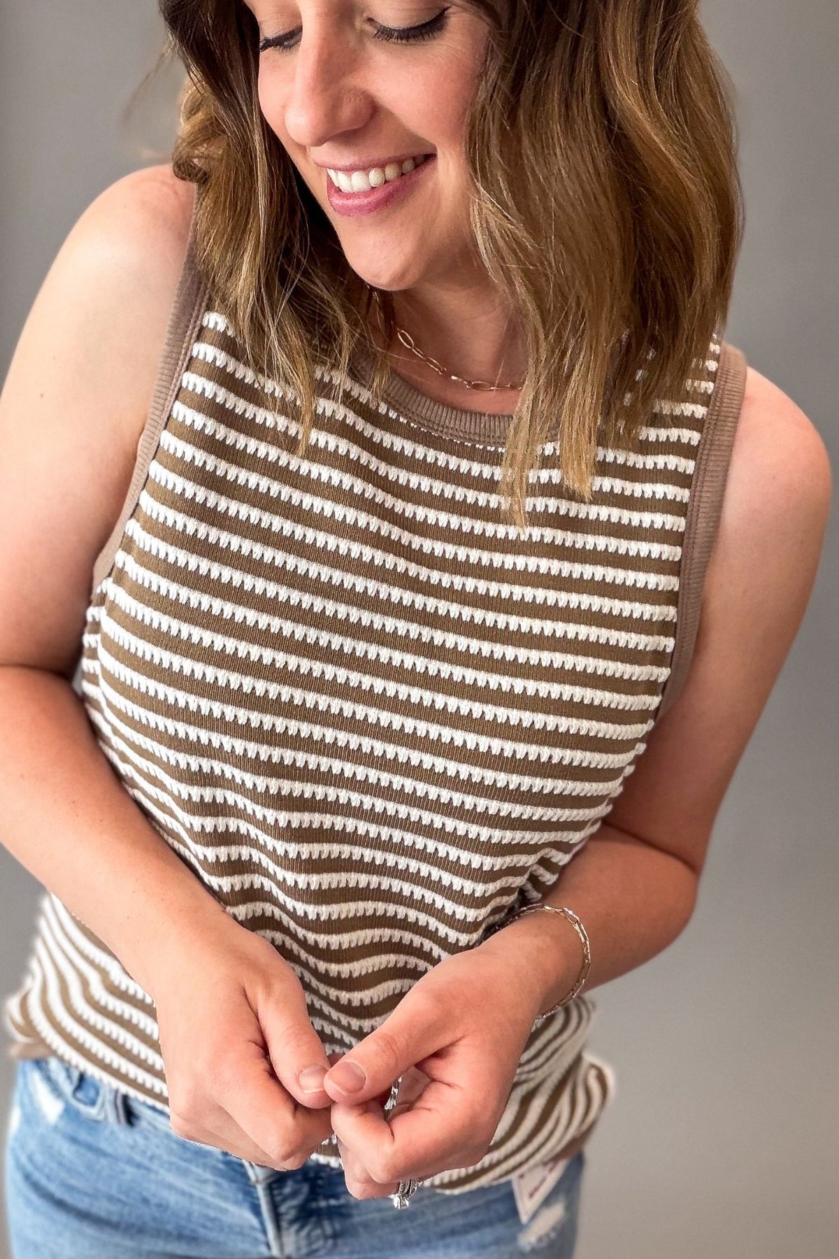 Woman wearing a striped sleeveless top and blue jeans against a gray background