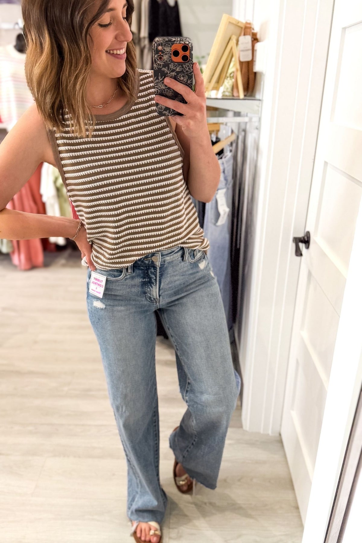 Woman taking a mirror selfie wearing a striped tank top and jeans in a store.