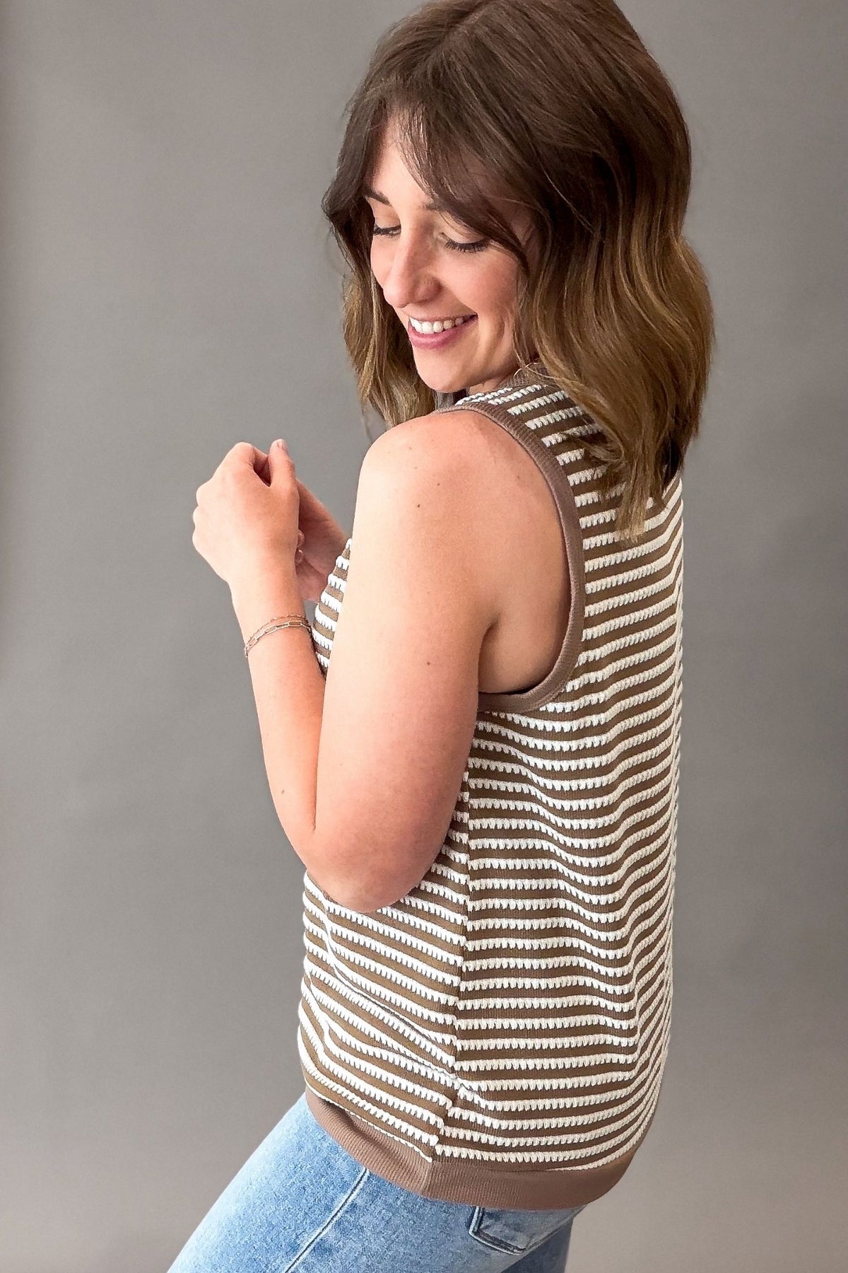 Woman wearing a striped sleeveless top and blue jeans against a gray background