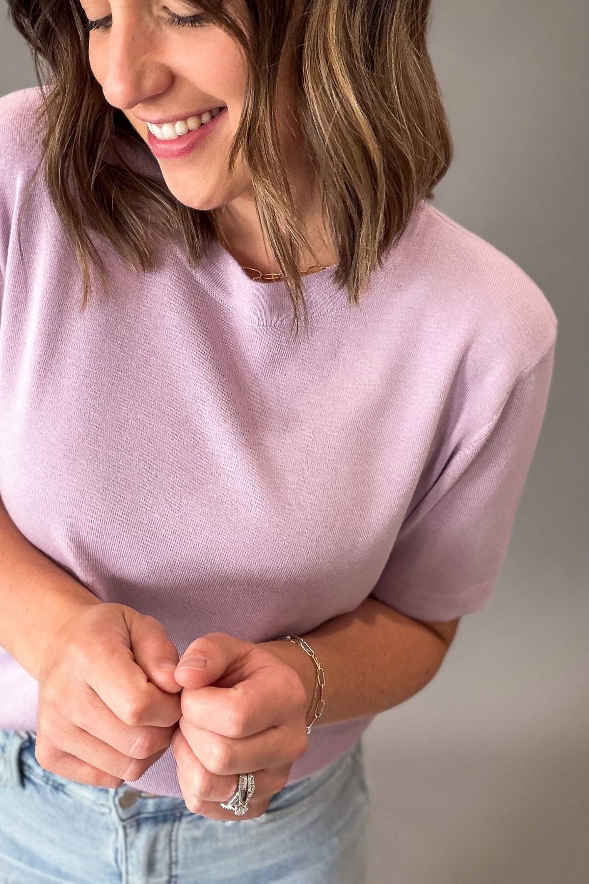 Woman wearing a light purple t-shirt and blue jeans against a neutral background