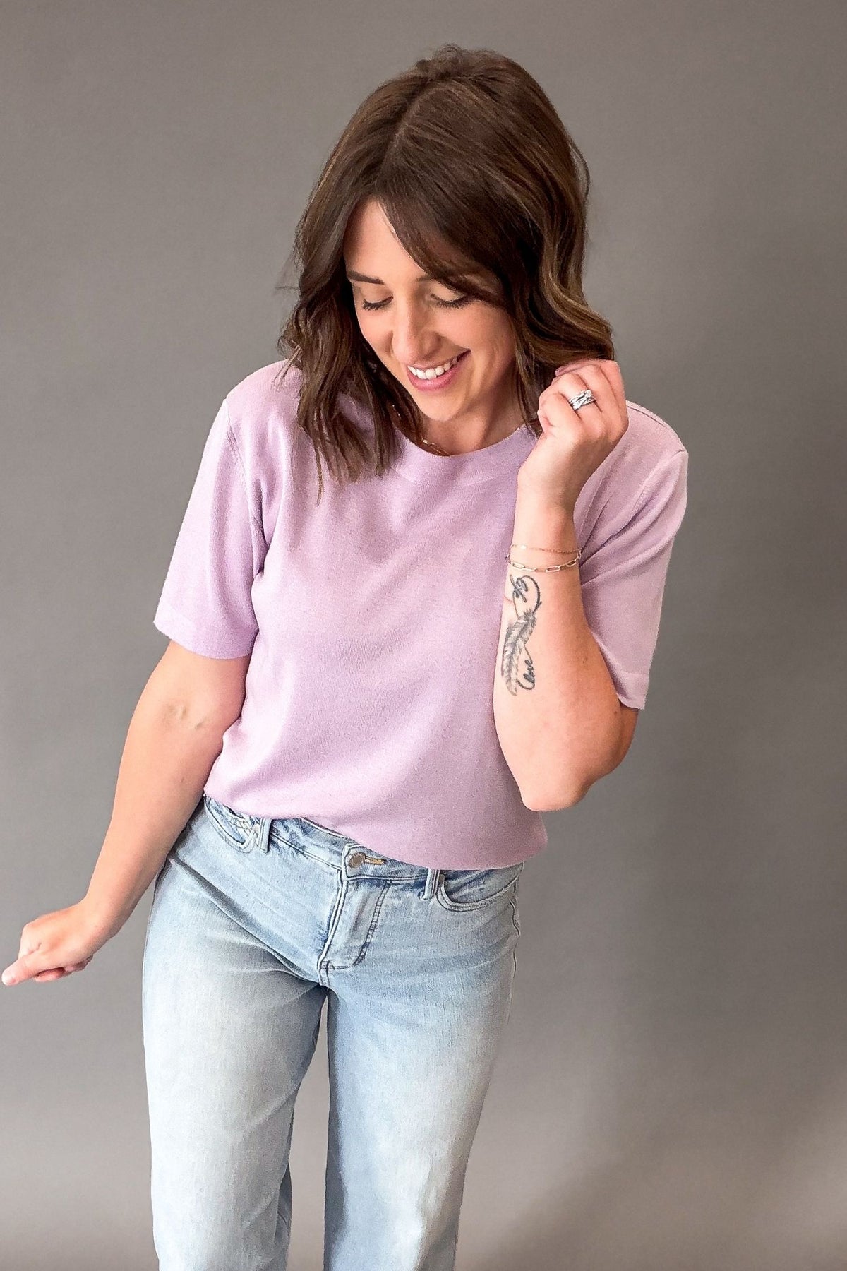 Woman wearing a light purple short sleeve and light blue jeans against a gray background
