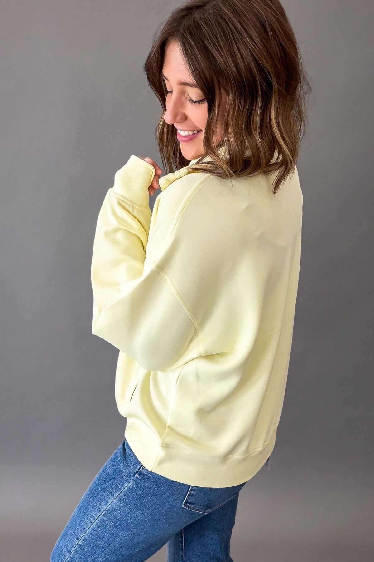 Woman wearing a light yellow oversized mock neck quarter zip and blue jeans against a gray background