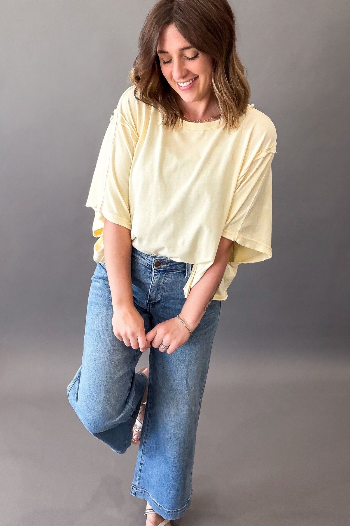 Woman wearing a light yellow top and blue jeans against a gray background