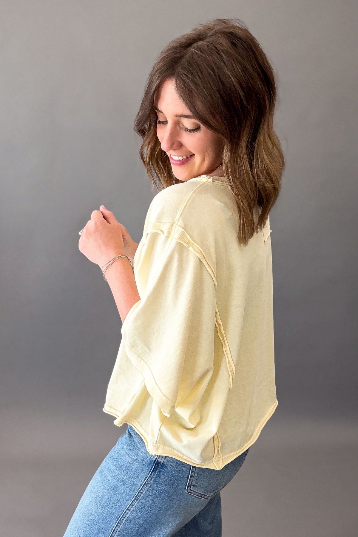 Woman wearing a light yellow basic short sleeve and blue jeans against a gray background