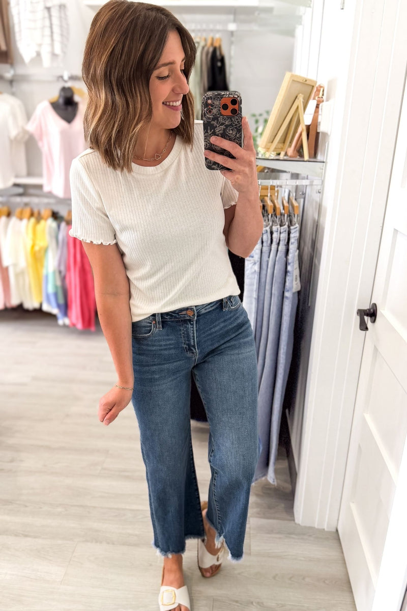 Woman taking a mirror selfie wearing a white t-shirt and blue jeans in a clothing store.