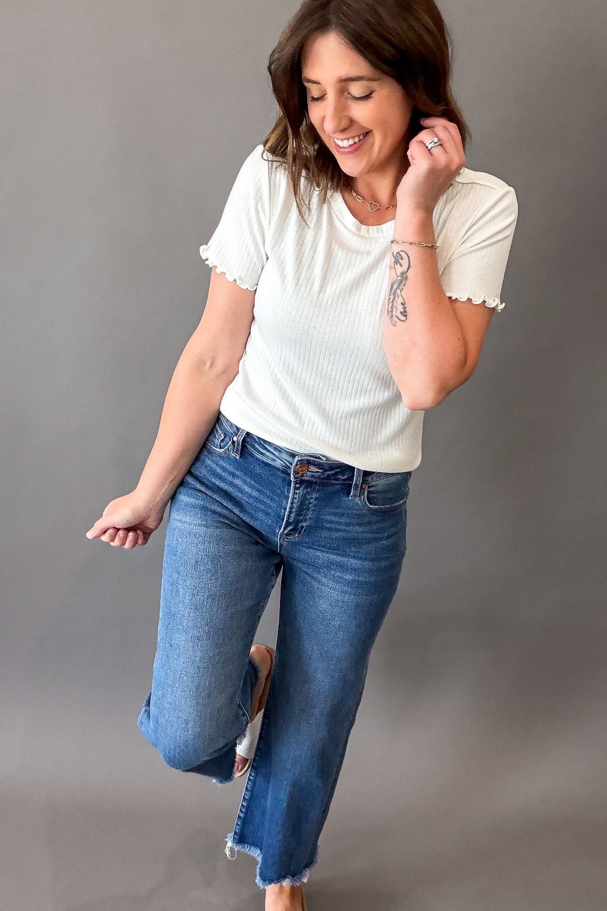 Woman wearing a white top and blue jeans against a gray background