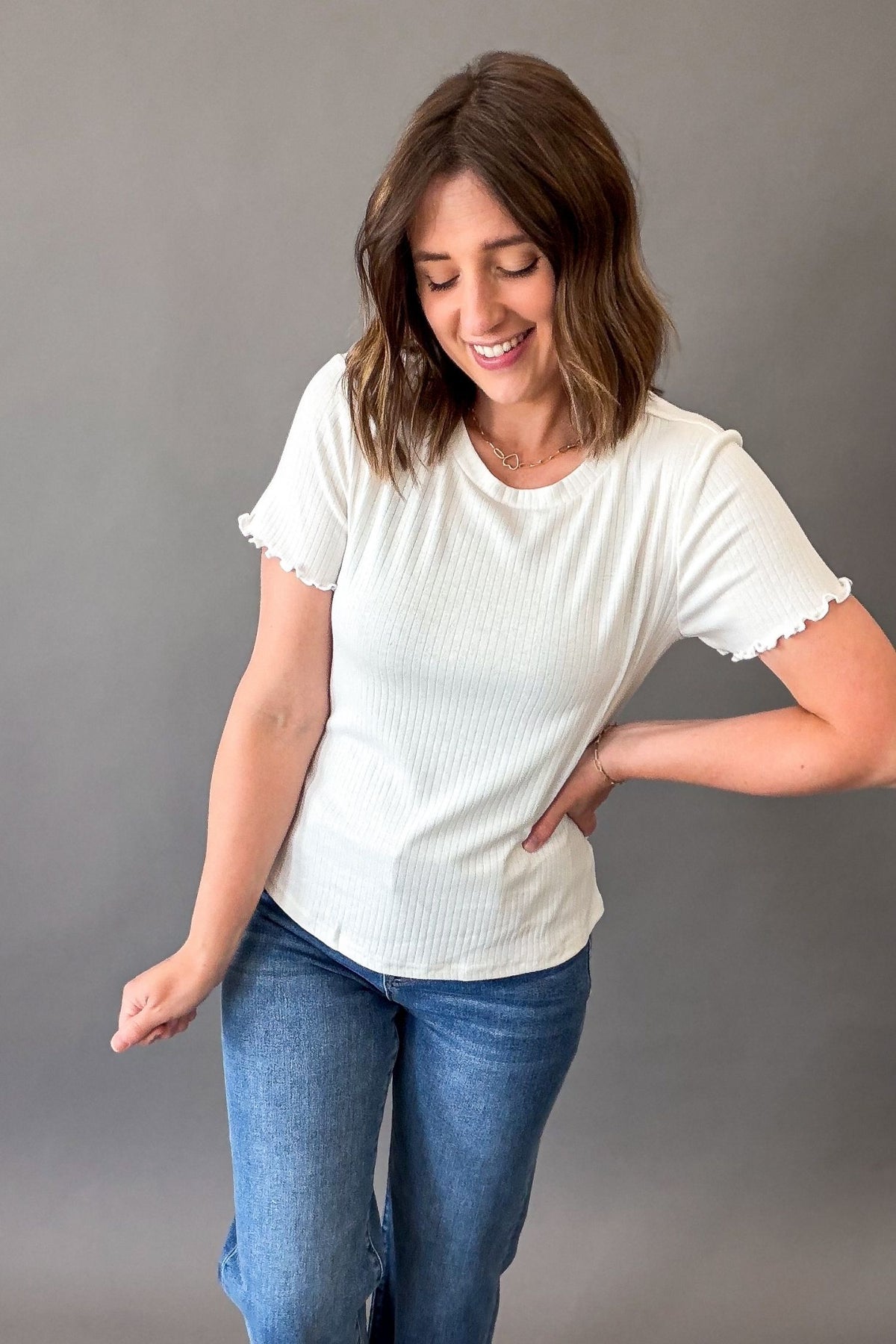 Woman wearing a white t-shirt and blue jeans against a gray background