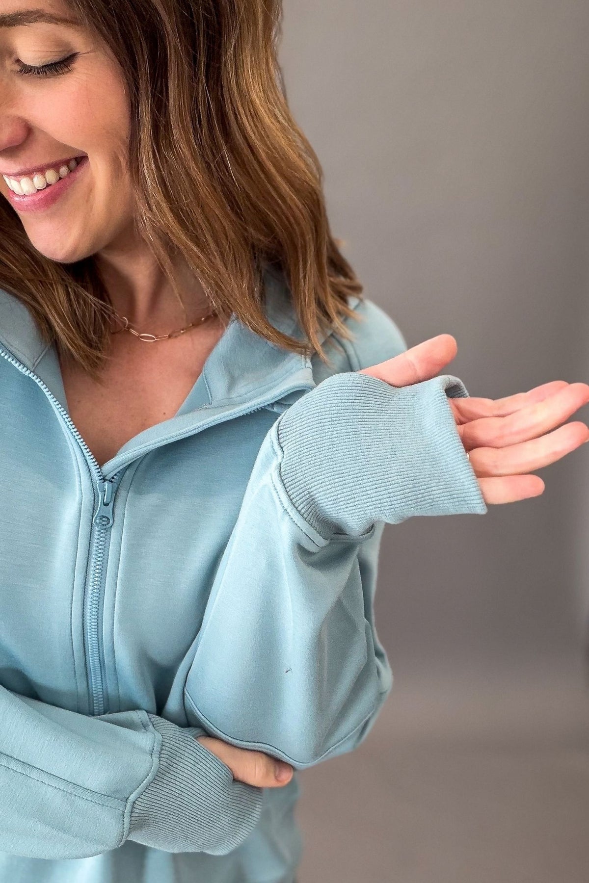 woman wearing a light blue half zip showing thumbholes and close up details against a dark grey background.