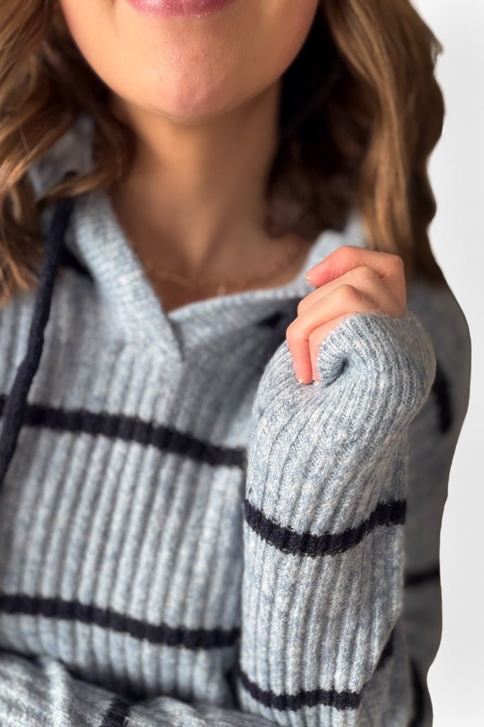 Close-up of a person wearing a light blue sweater hoodie with dark navy blue stripes on a white background