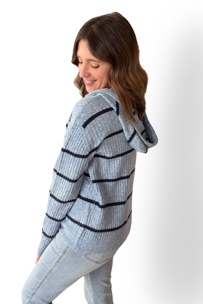 Woman wearing a light blue sweater hoodie and dark navy striped sweater on a white background